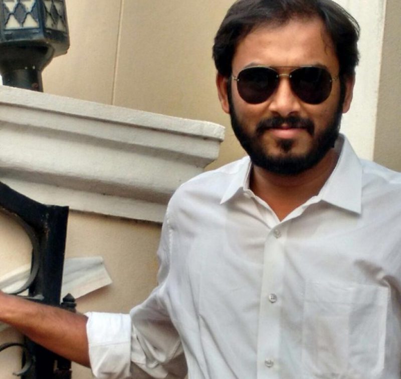 Man in sunglasses and white shirt smiling outdoors.