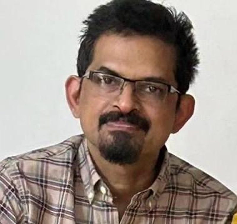 Portrait of a man with glasses and a beard wearing a checkered shirt.